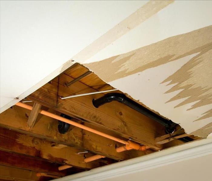 An open ceiling with exposed piping and water damage. 